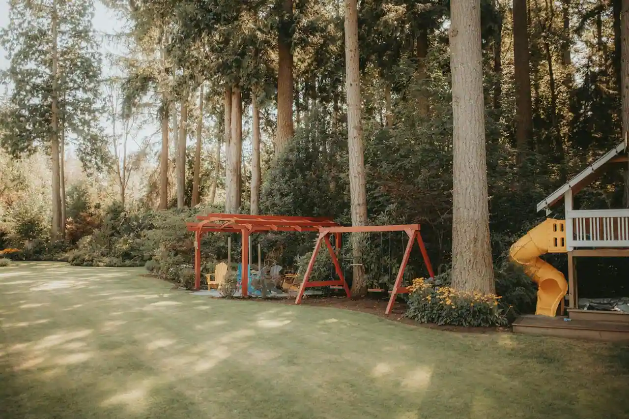 Aire de jeu en bois dans un jardin avec portique, toboggan et sol amortissant en copeaux