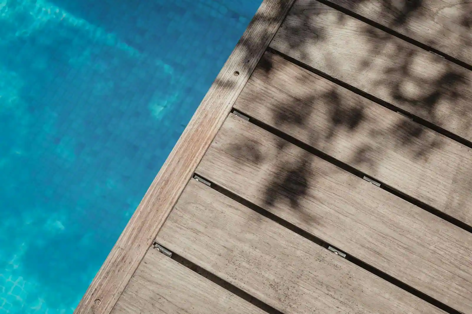 Terrasse extérieure en bois naturel longeant une piscine dans un jardin verdoyant, mobilier d'extérieur visible