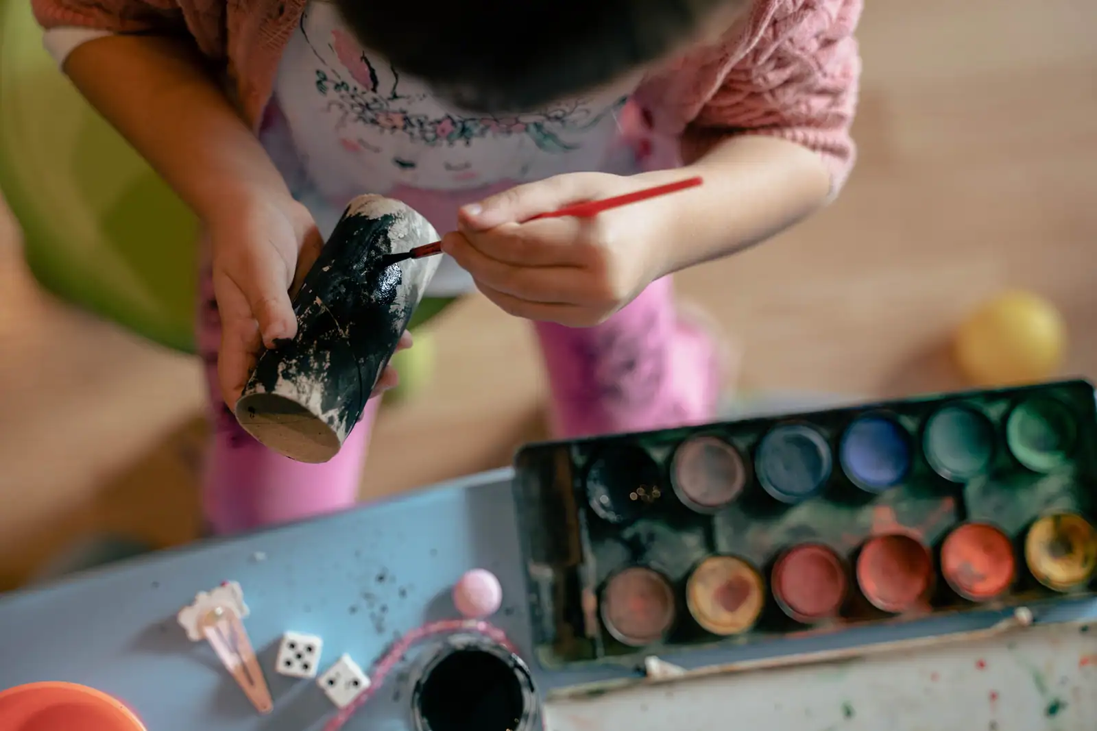 Un enfant peint un rouleau en carton au pinceau, à côté d'une palette de peinture.