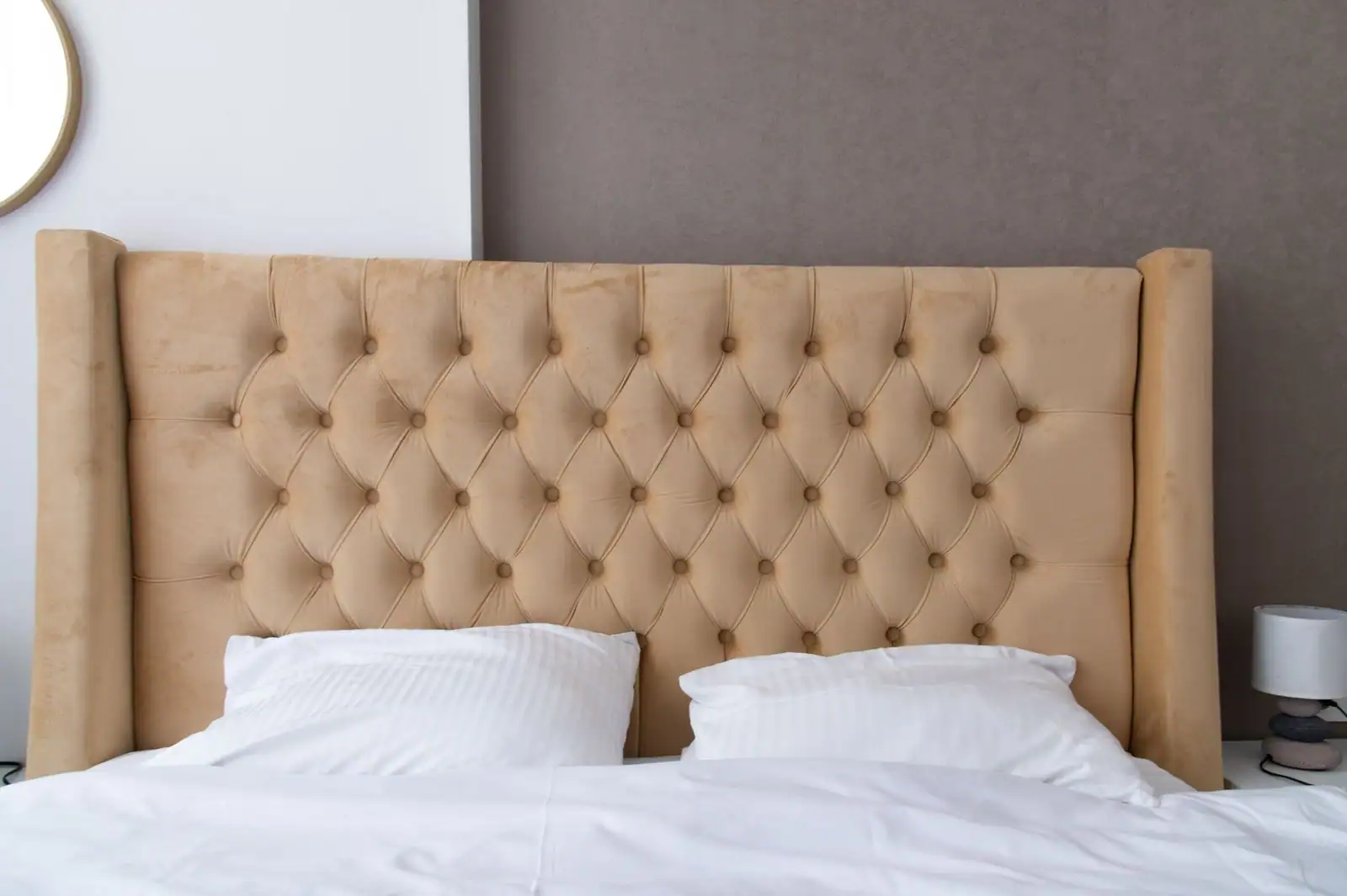 Chambre aux tons neutres avec grande tête de lit capitonnée beige et linge de lit blanc