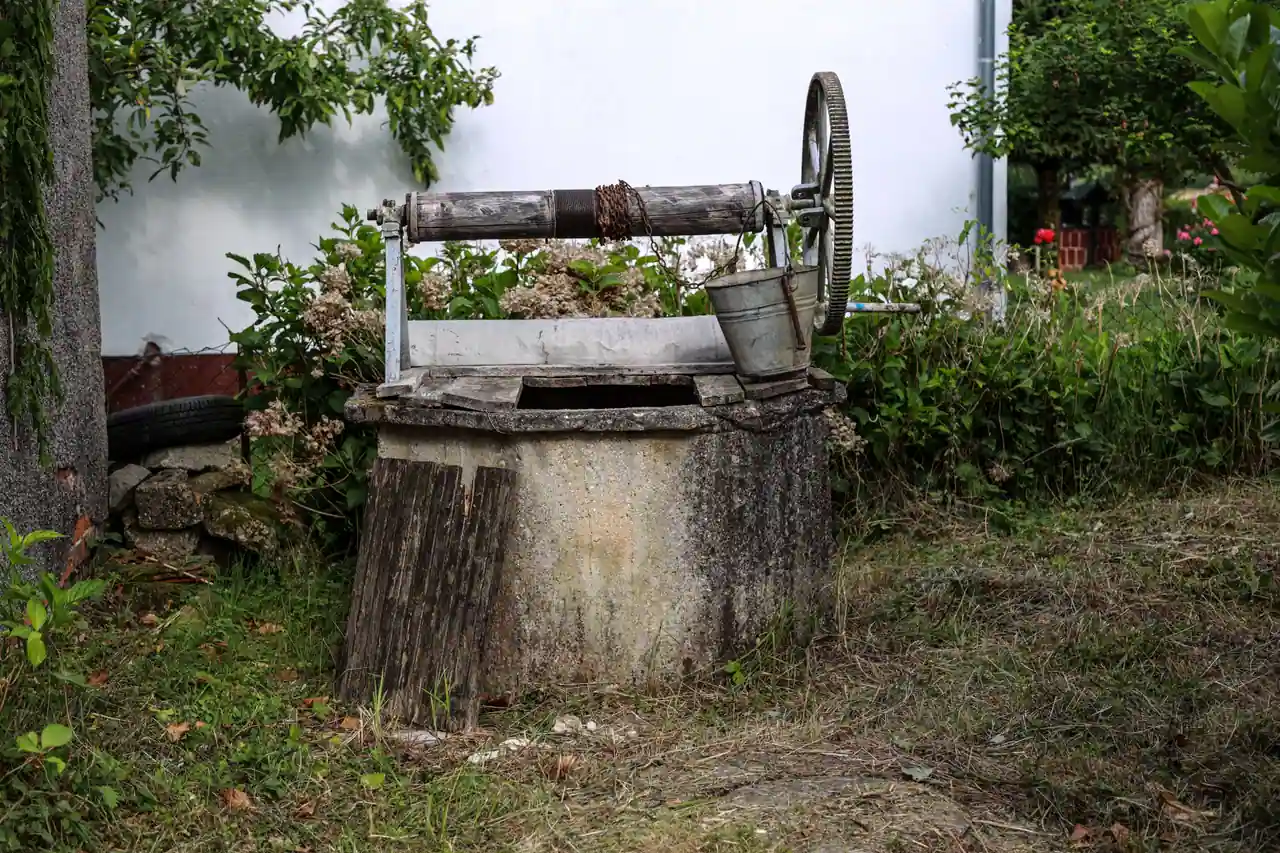 Puits traditionnel en pierre dans un jardin, avec son treuil à manivelle et un seau métallique