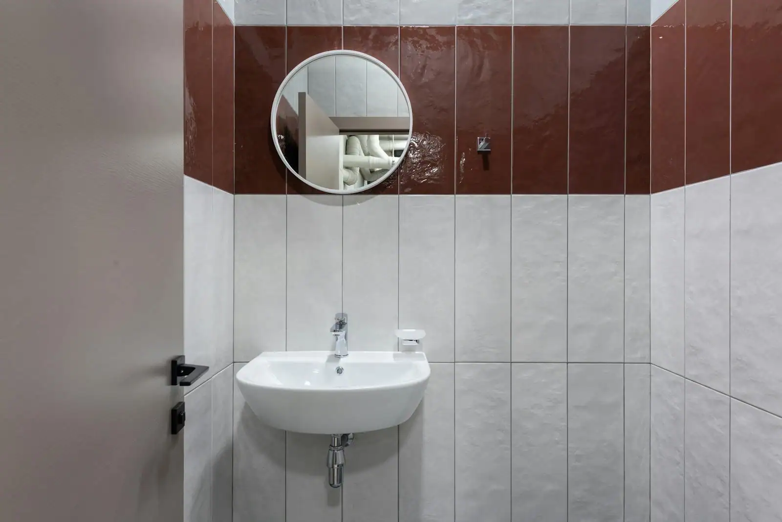 Salle de bain carrelée avec vasque suspendue blanche et miroir rond