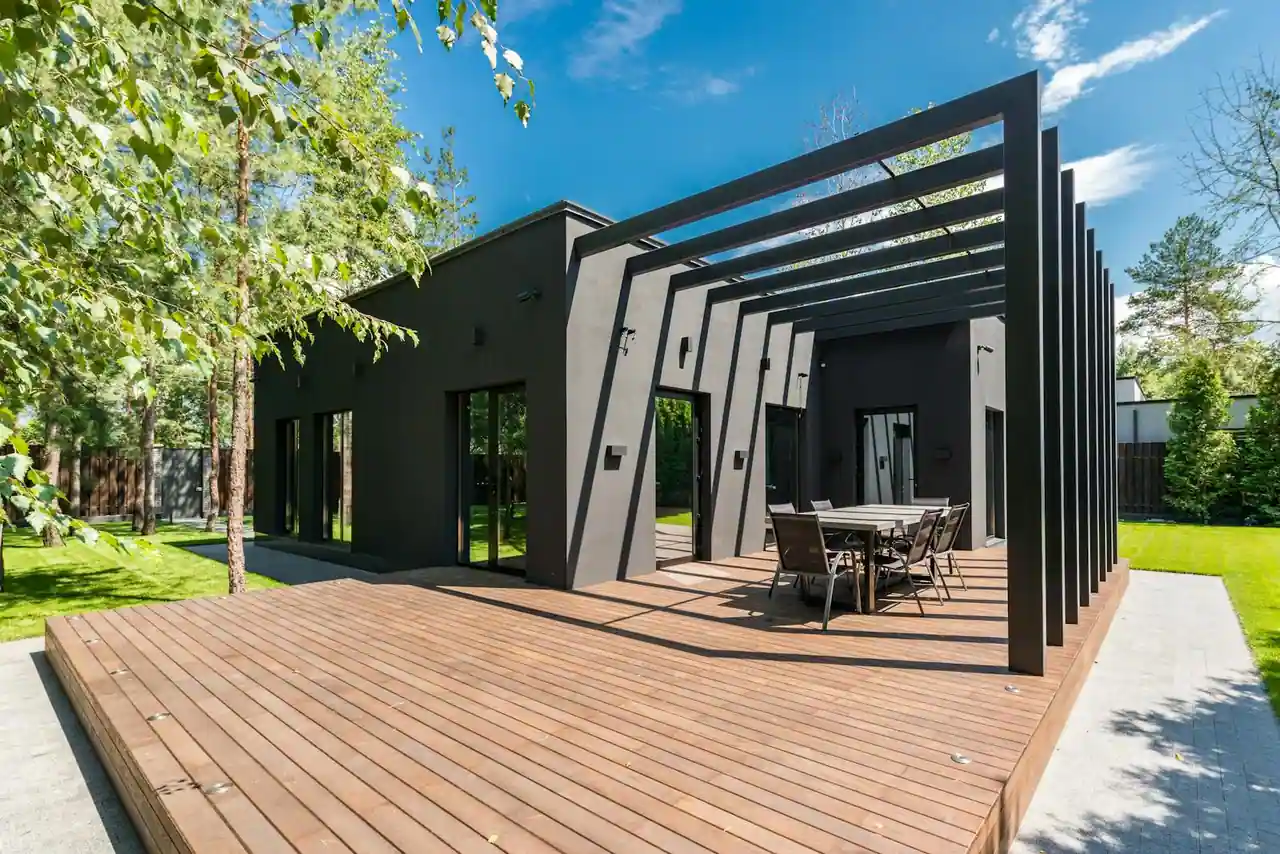 Terrasse en lames de bois clair dans un jardin ensoleillé, avec pergola et salon de jardin