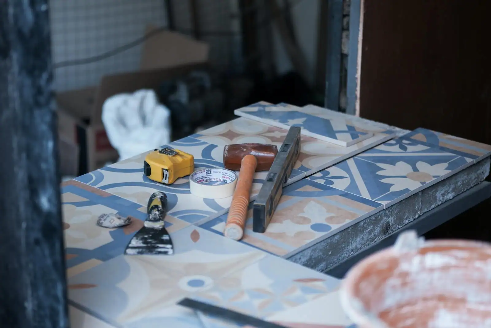 Outils de pose posés sur des carreaux de ciment à motifs : mètre ruban, maillet et règle métallique