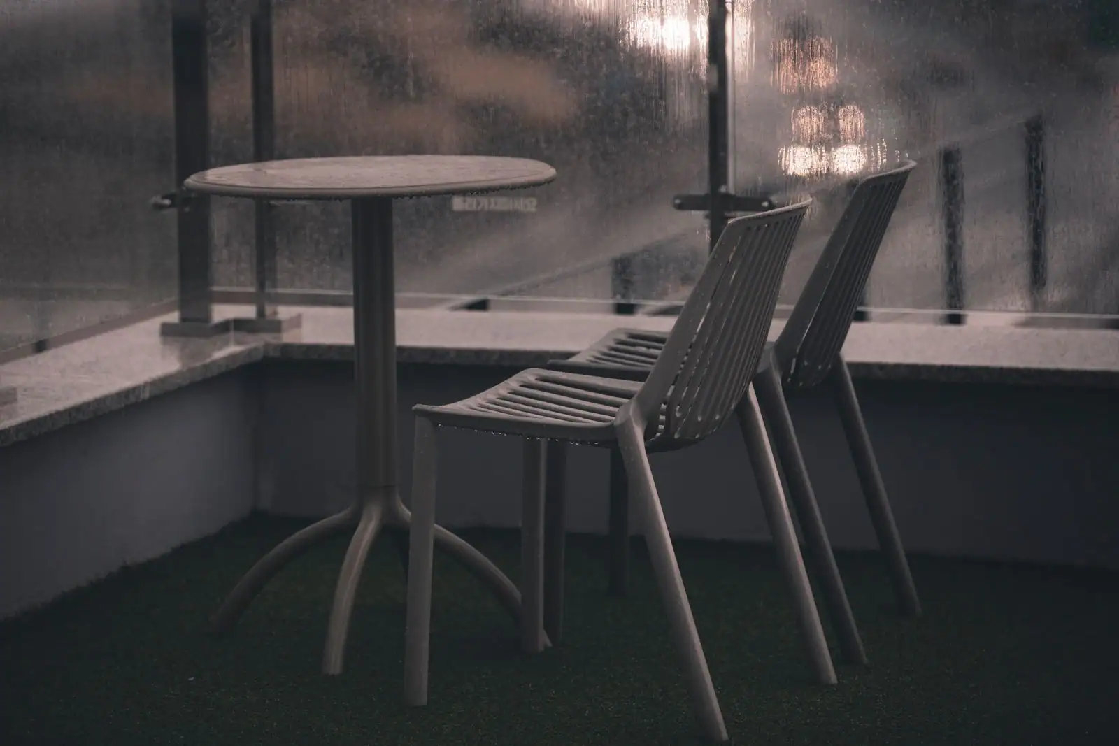 Table et chaises de jardin en résine sur une terrasse abritée, derrière une paroi vitrée.