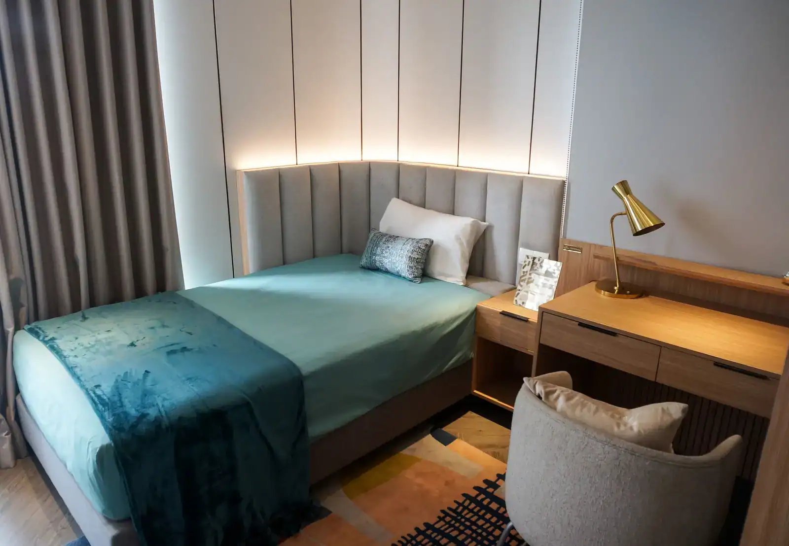 Chambre single compacte avec lit simple, bureau en bois et lampe, aménagée pour une personne.