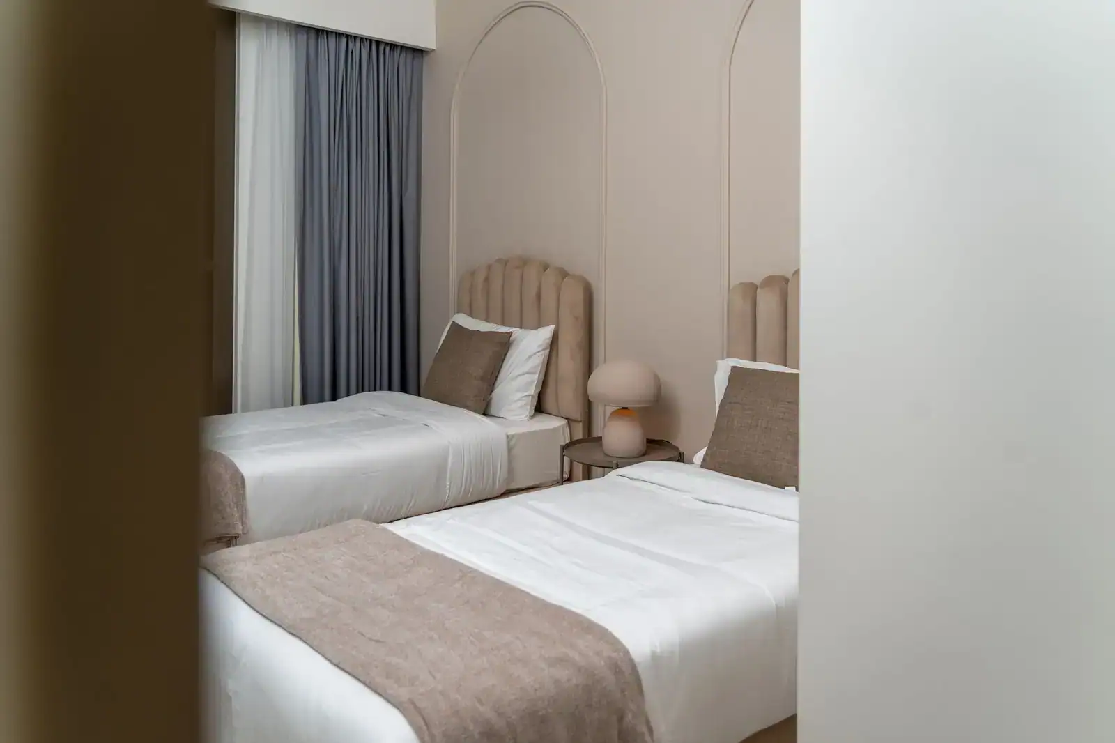 Chambre d'hôtel avec deux lits simples séparés à têtes de lit capitonnées, réunis par une table de nuit.