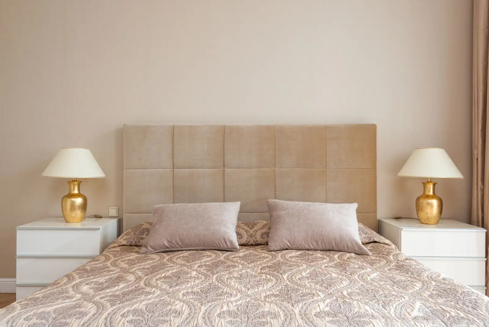 Chambre avec tête de lit capitonnée beige, grand lit et deux tables de chevet symétriques éclairées