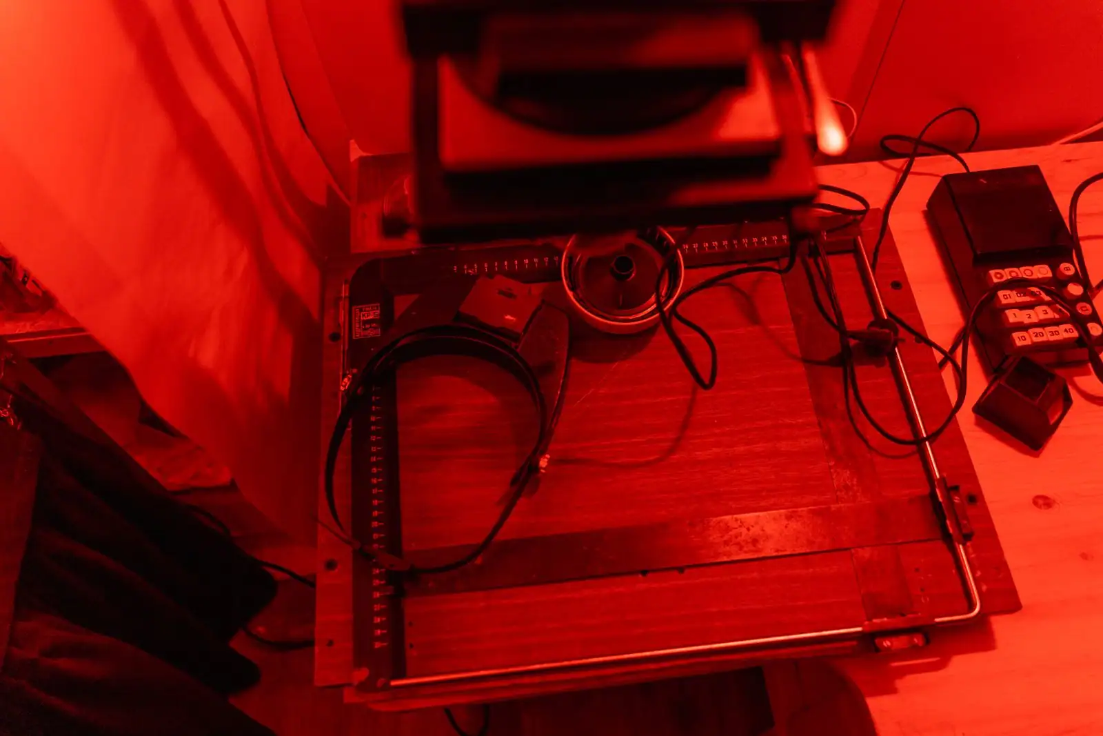 Laboratoire photo argentique éclairé en rouge : agrandisseur, margeur et minuterie de tirage