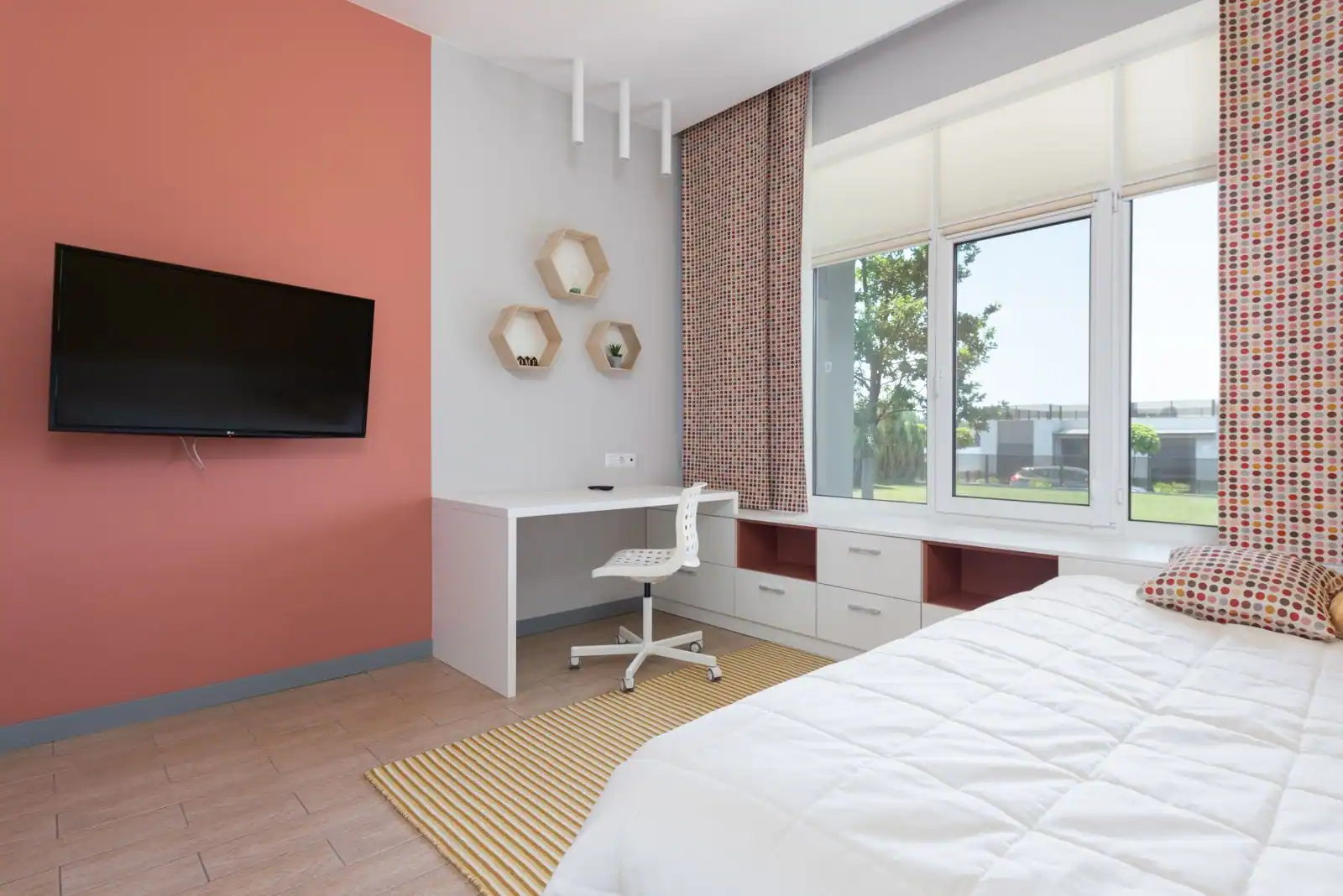 Chambre meublée avec un lit, un bureau blanc et des étagères murales près d'une grande fenêtre
