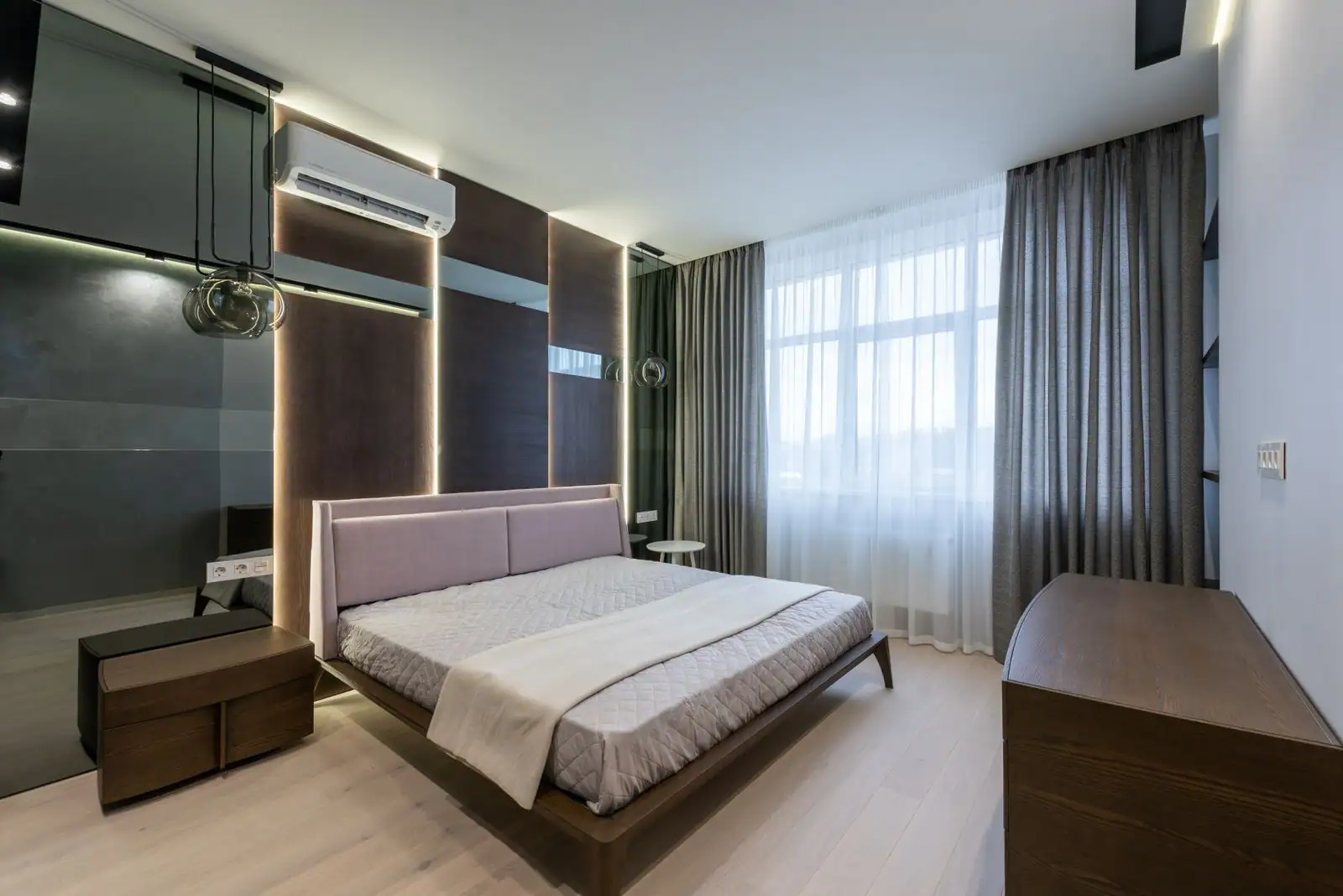 Chambre moderne et lumineuse avec lit, mobilier en bois et lumière du jour tamisée par de longs rideaux.