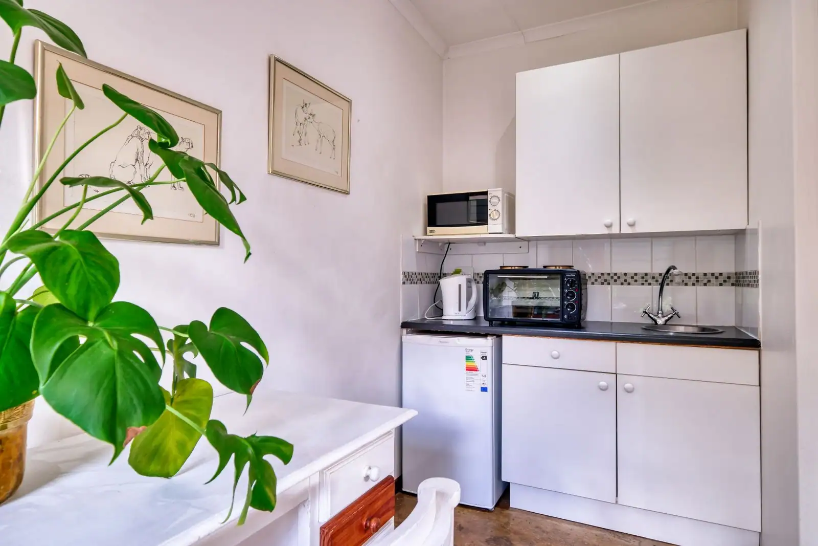 Petite kitchenette de studio : plan de travail avec évier, meubles blancs, micro-ondes et mini-four