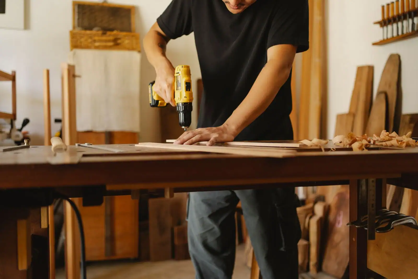 Menuisier perçant une planche de bois à la perceuse sans fil sur un établi d’atelier.