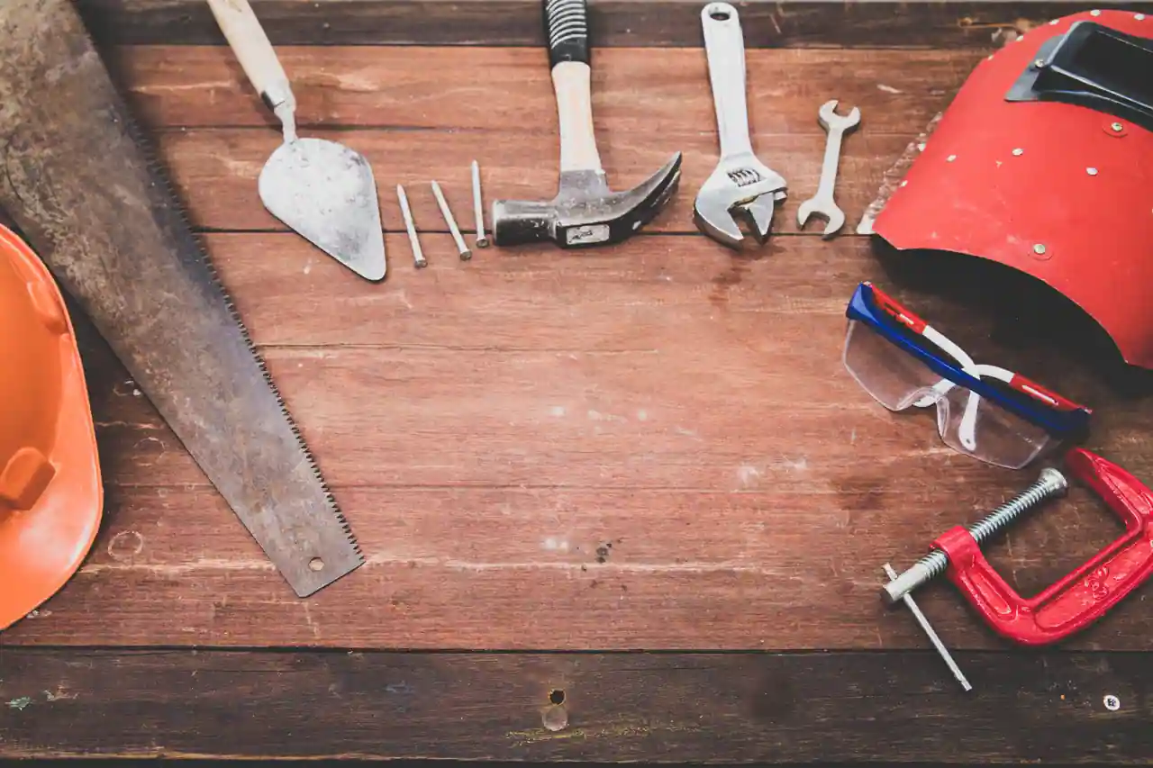 Outils de bricolage disposés sur un plan de travail en bois : scie, marteau, clés et protections.