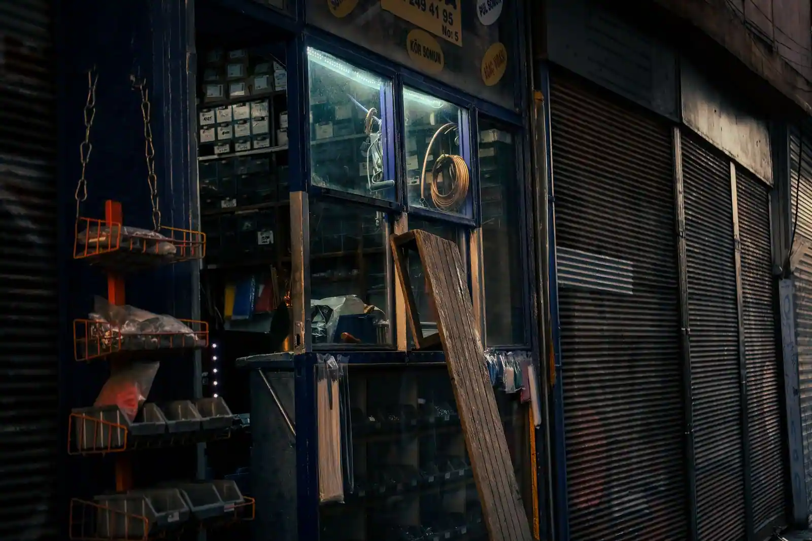 Devanture d’une ancienne quincaillerie au rideau métallique partiellement baissé, outils en vitrine.