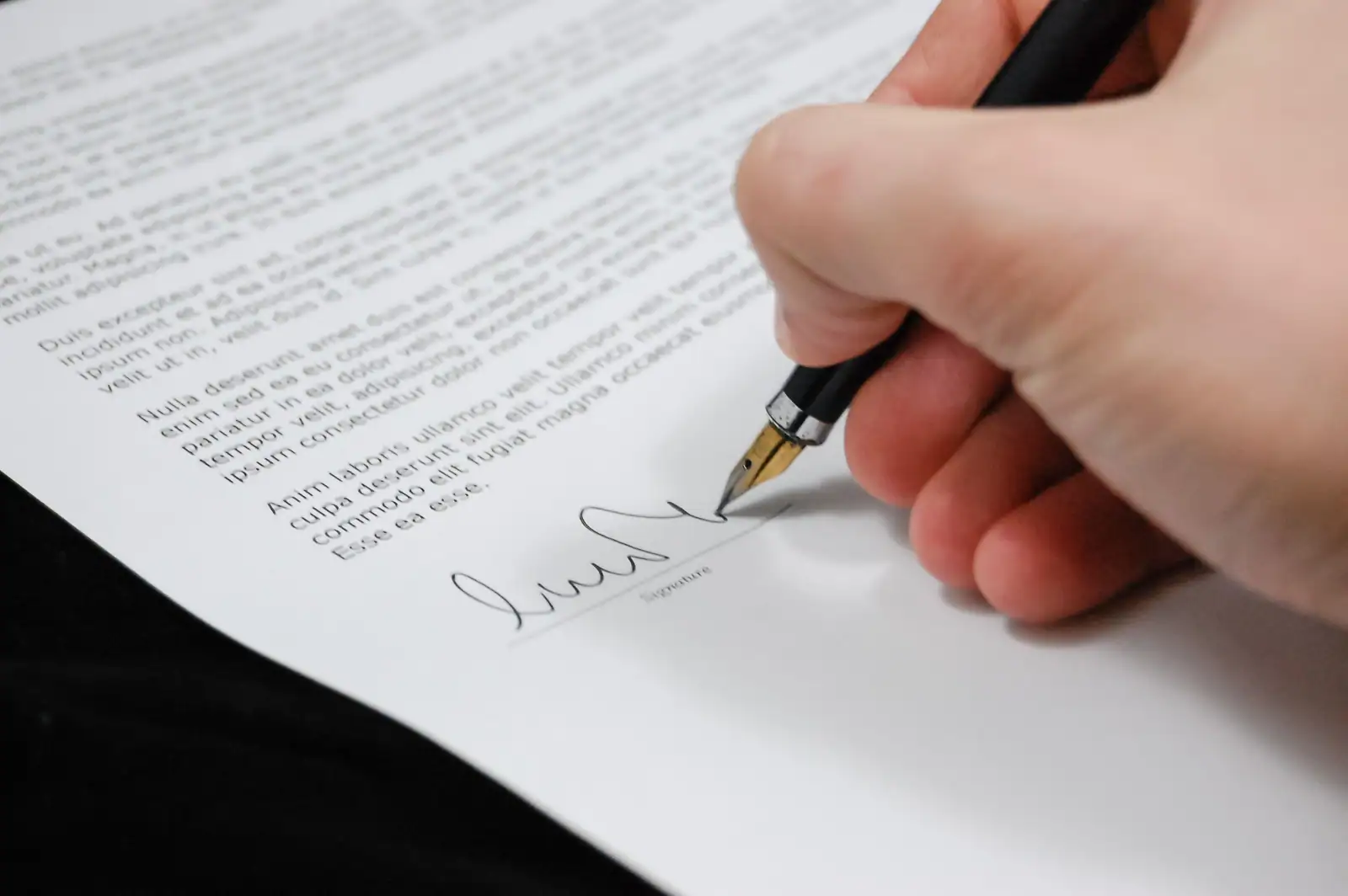 Main signant un document au stylo plume, sur une feuille imprimée portant une ligne de signature.