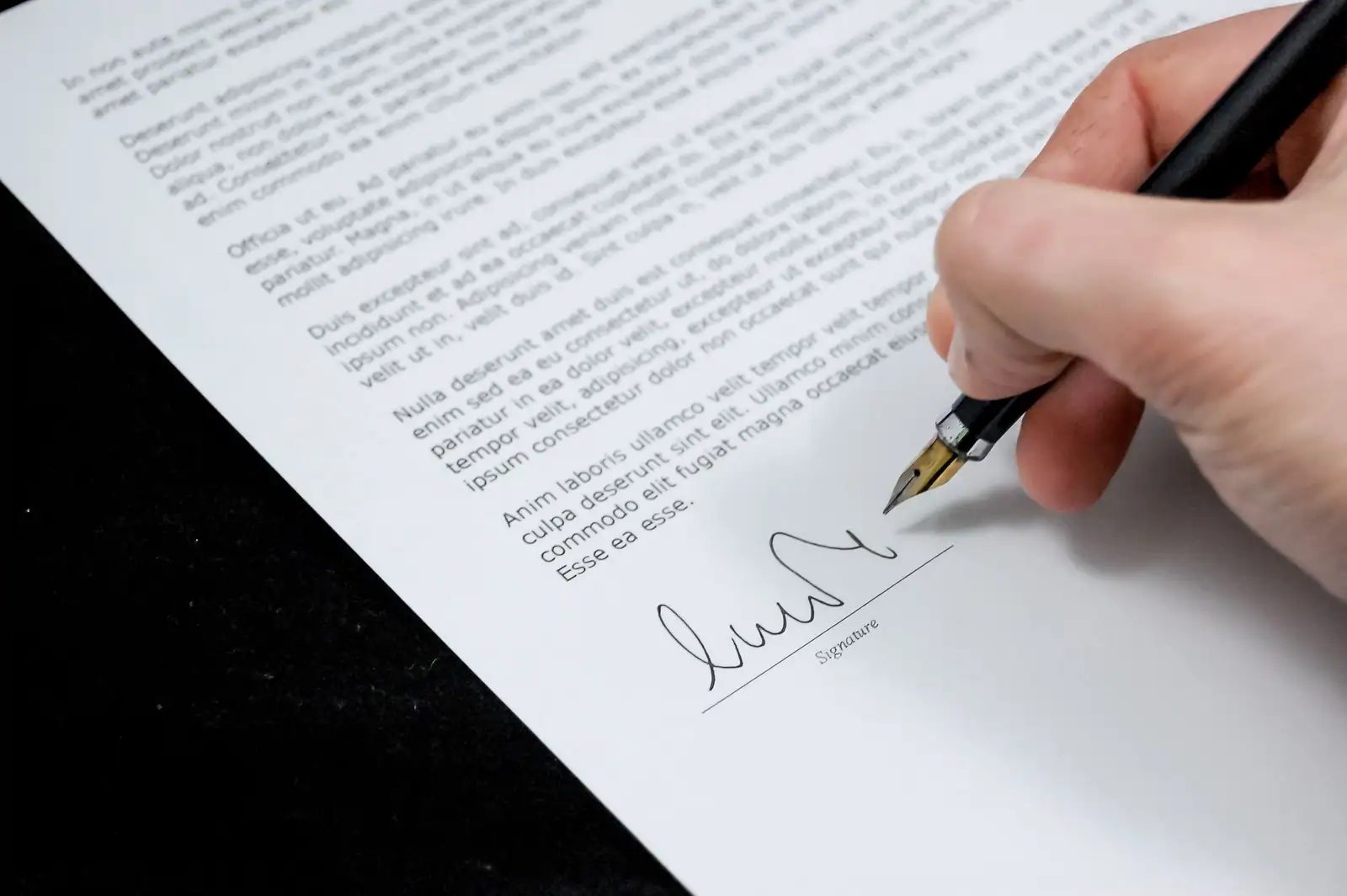 Main signant un document officiel au stylo plume, sur la ligne de signature d’un acte.