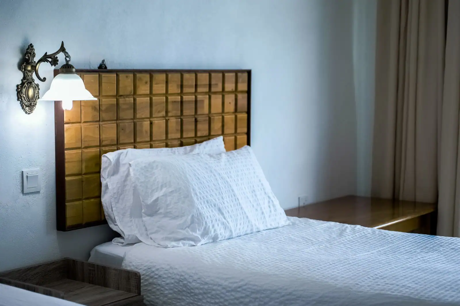 Chambre à l'ambiance hôtelière : lit habillé de linge blanc, applique de chevet et palette claire