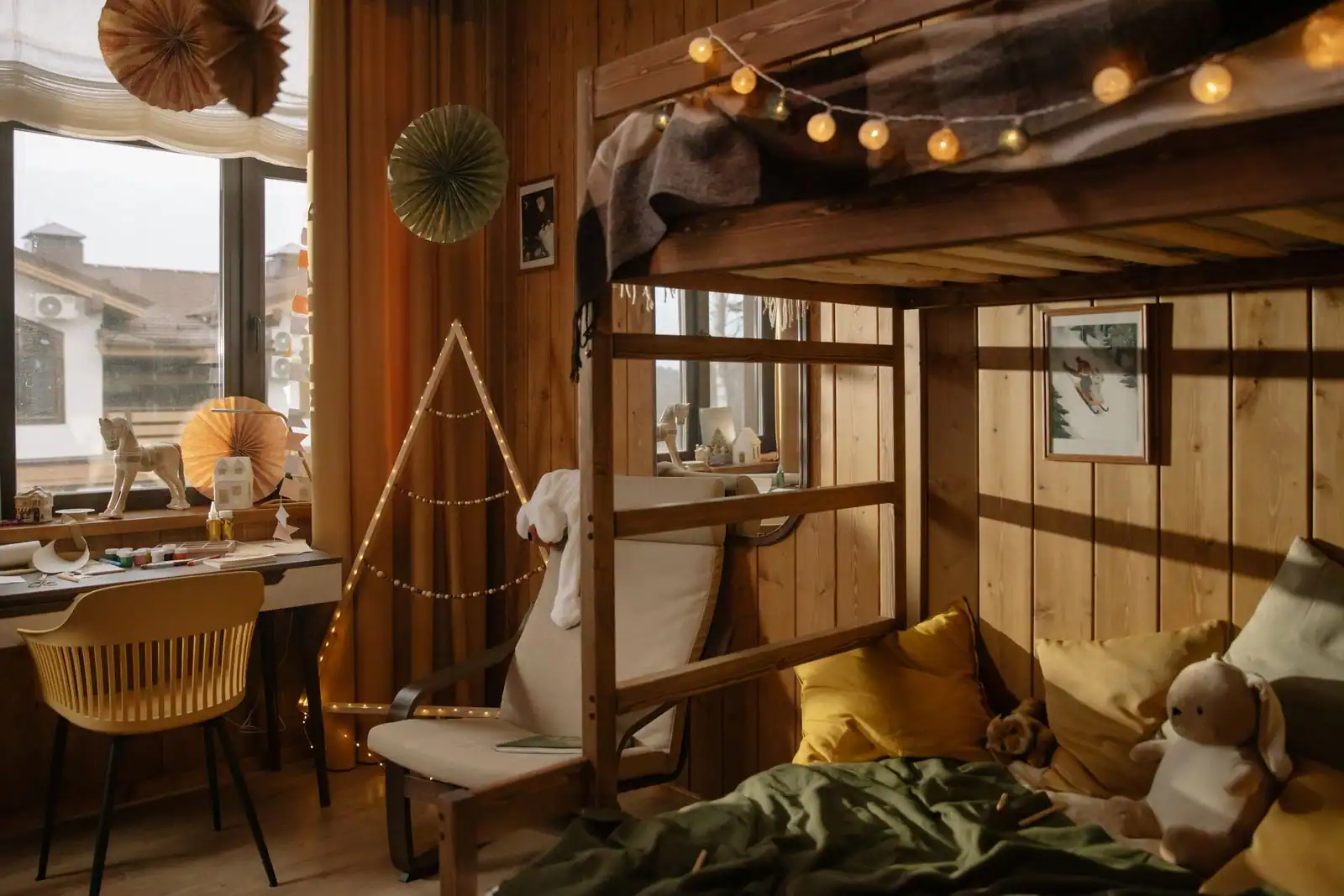Chambre d’enfants chaleureuse avec lit mezzanine en bois, coin bureau et guirlande lumineuse.
