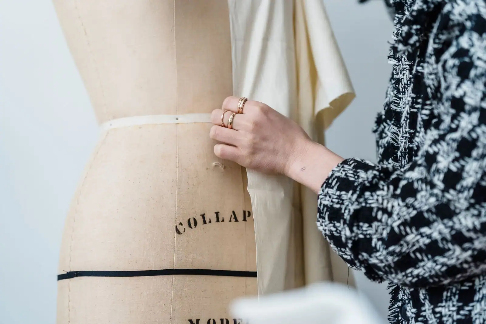 Main drapant un tissu écru sur un mannequin de couturier en toile, dans un atelier de haute couture.