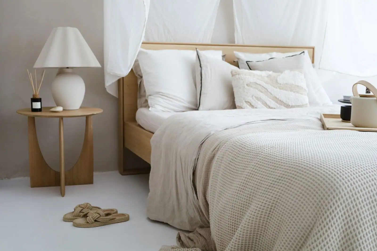 Chambre aux tons neutres et chauds, literie en lin froissé et mobilier en bois clair.