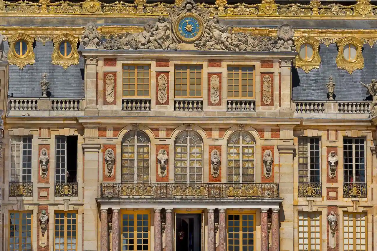 Façade richement ornée du château de Versailles, avec ses décors dorés et son horloge, côté cour de Marbre.