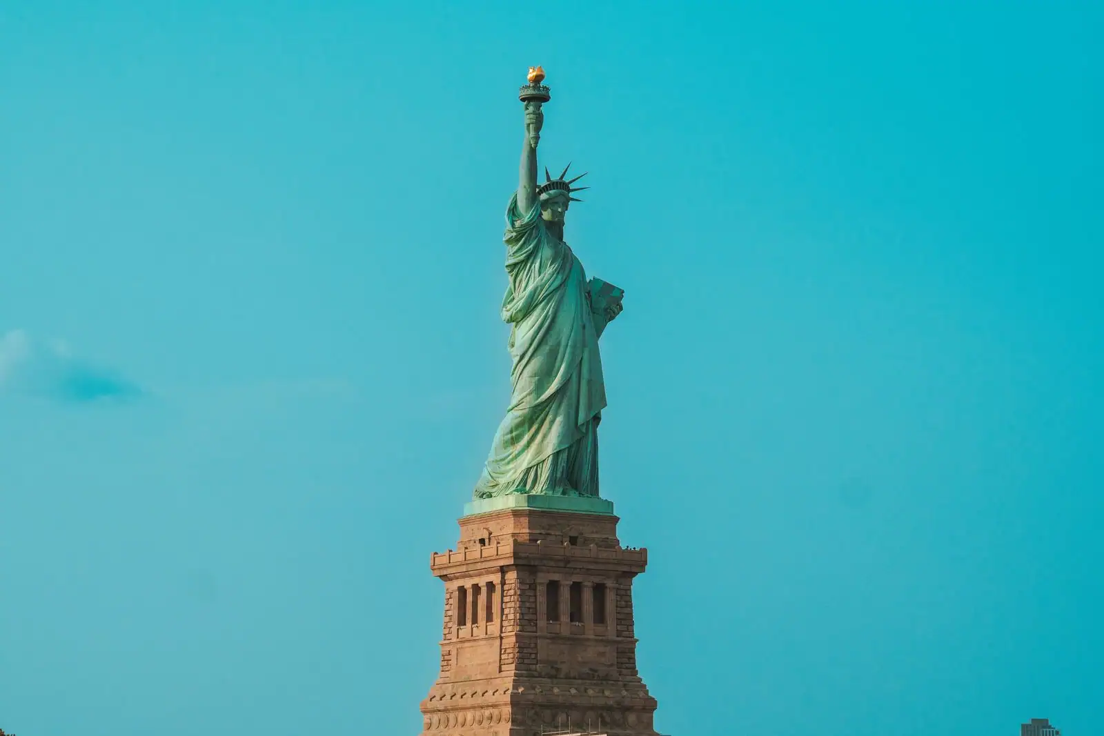 La statue de la Liberté, monument de cuivre patiné vert-de-gris, sur son socle, torche levée vers le ciel.