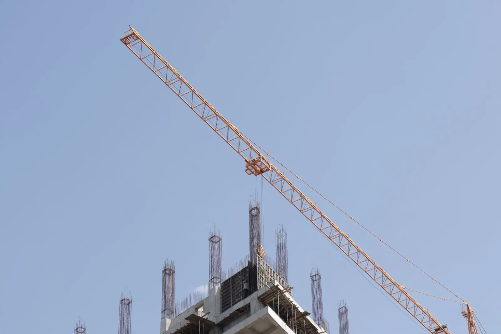 Grue de chantier au-dessus d'un bâtiment en construction, dont le sommet en béton hérisse d'armatures d'acier.