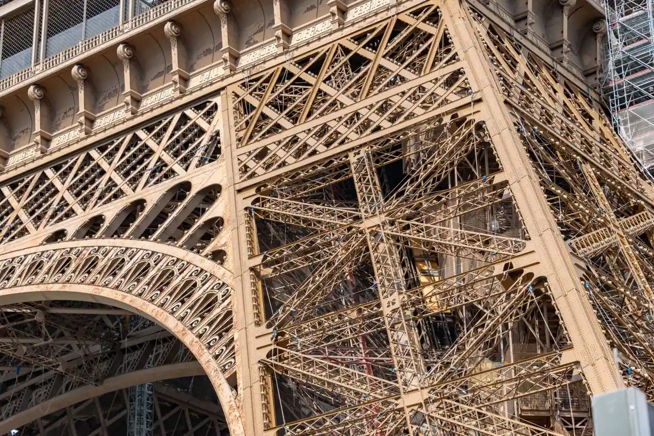 Gros plan sur l'armature de fer ajourée de la tour Eiffel, avec ses arches et ses poutrelles rivetées.