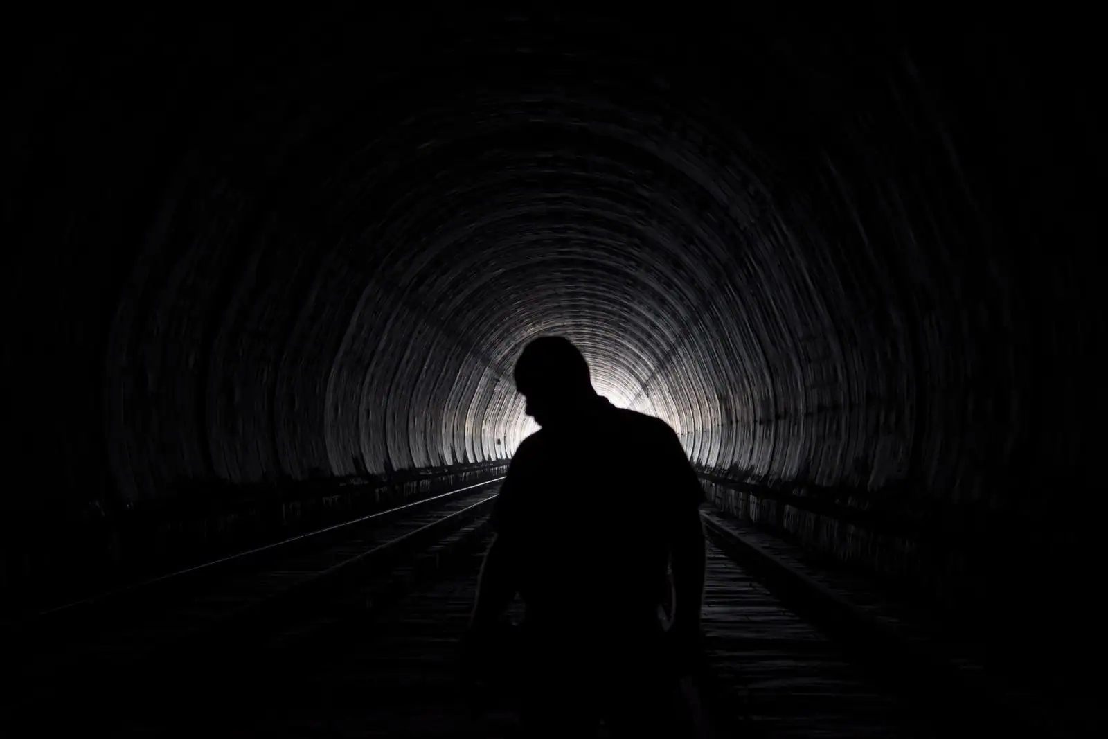 Intérieur voûté d'un tunnel ferroviaire, silhouette d'une personne marchant vers la lumière au bout