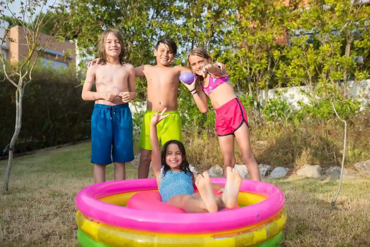 Enfants jouant autour d’une petite piscine gonflable dans un jardin en été
