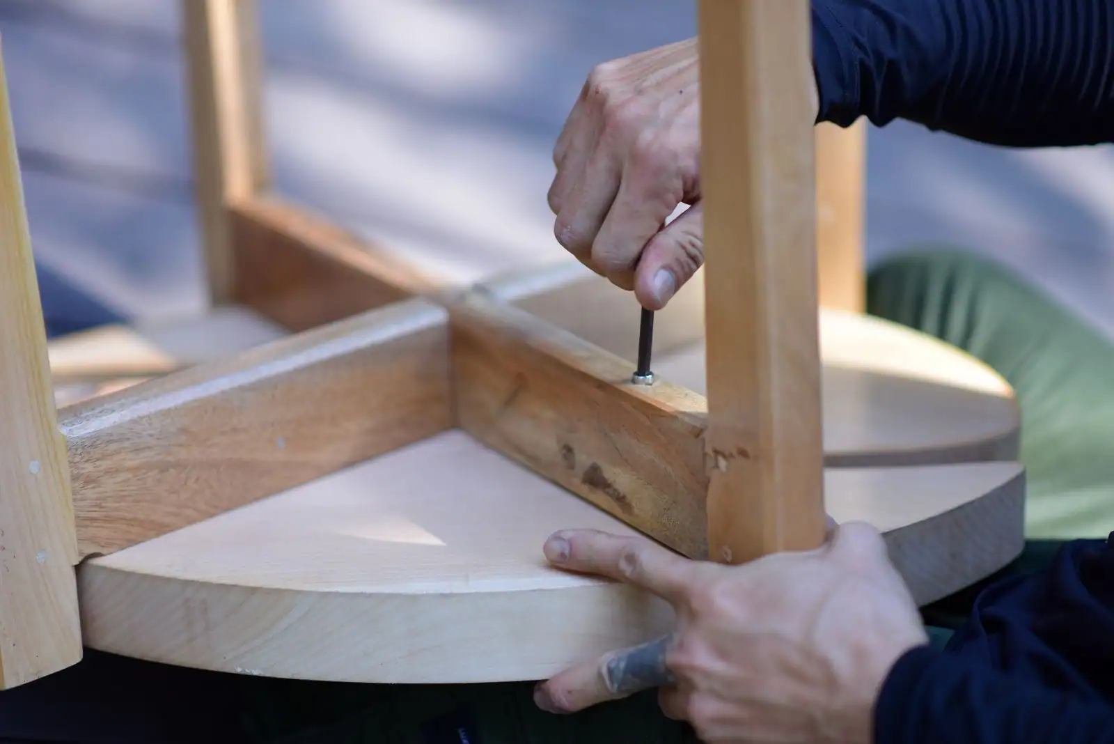 Mains vissant l'assemblage d'un tabouret en bois clair retourné, à l'aide d'un tournevis