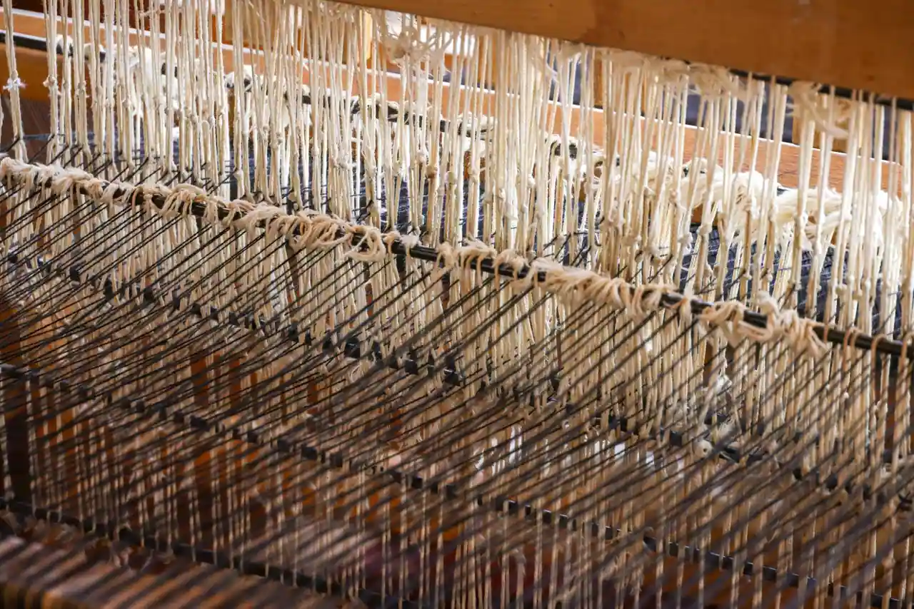 Métier à tisser traditionnel en bois, fils de laine clairs tendus, gros plan sur l'ouvrage en cours.