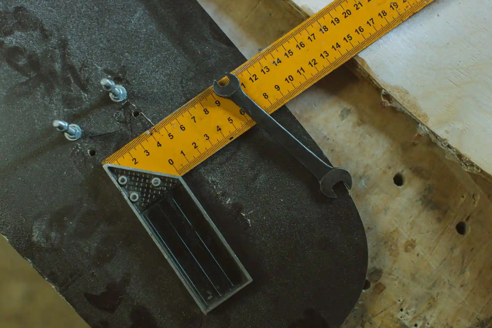 Une clé plate et un mètre pliant jaune gradué posés sur une planche en bois, dans un atelier.