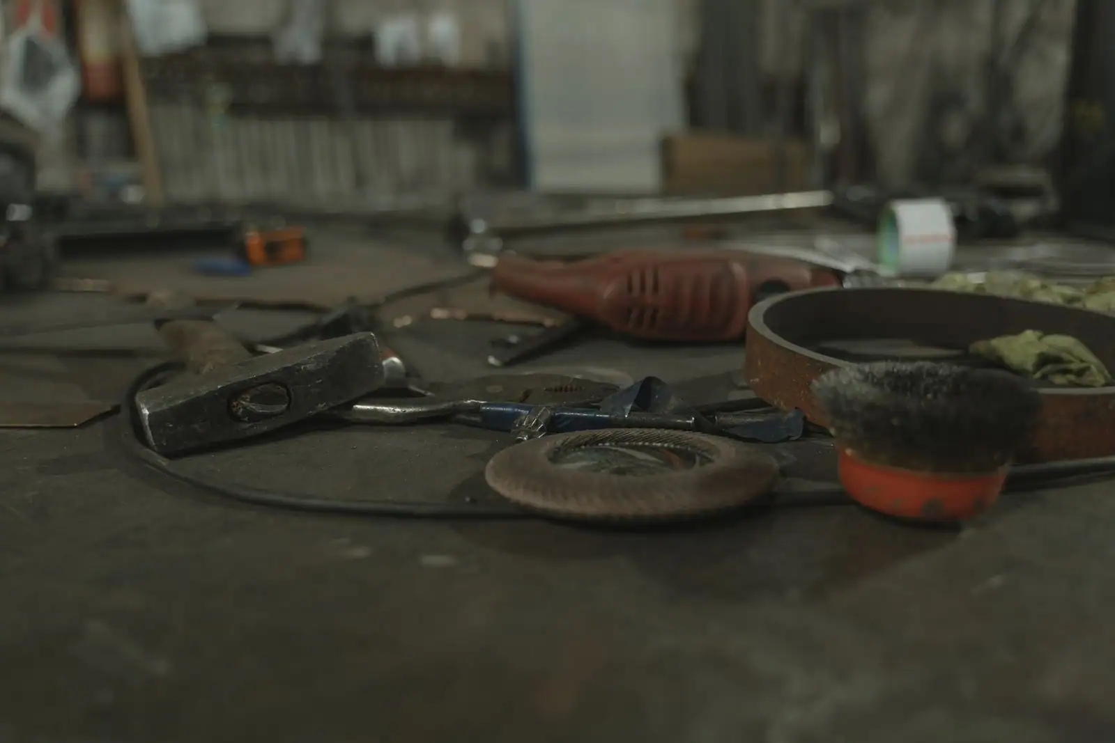 Assortiment d'outils de bricolage usagés sur un établi d'atelier : marteau, clé et outil électroportatif.